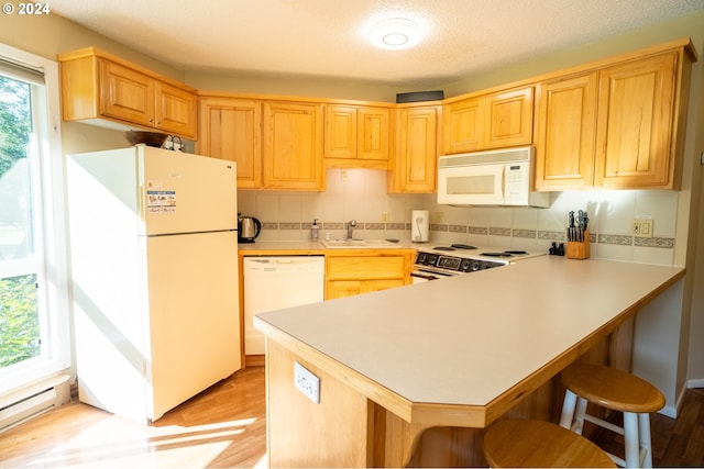 kitchen with sink, white appliances, light hardwood / wood-style floors, kitchen peninsula, and a breakfast bar