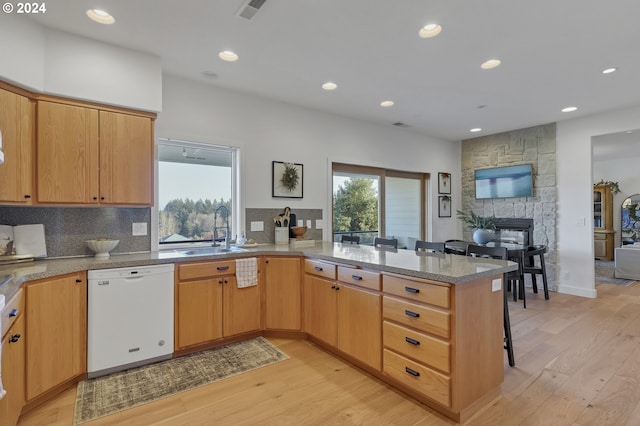 kitchen with kitchen peninsula, sink, light hardwood / wood-style flooring, dishwasher, and a breakfast bar area