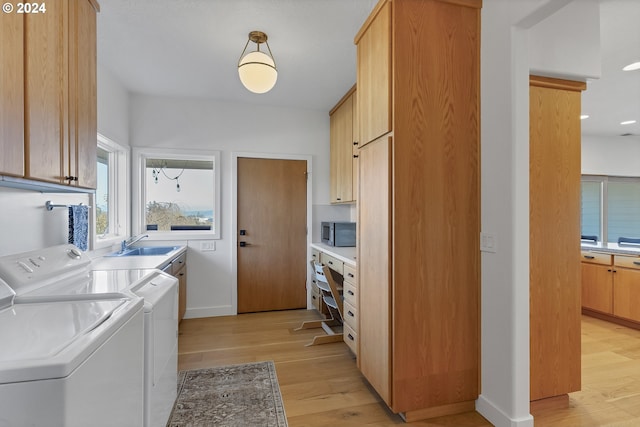 washroom with cabinets, washing machine and clothes dryer, sink, and light hardwood / wood-style flooring