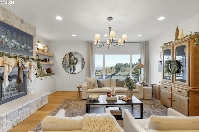 living room featuring a chandelier, light hardwood / wood-style flooring, and a stone fireplace