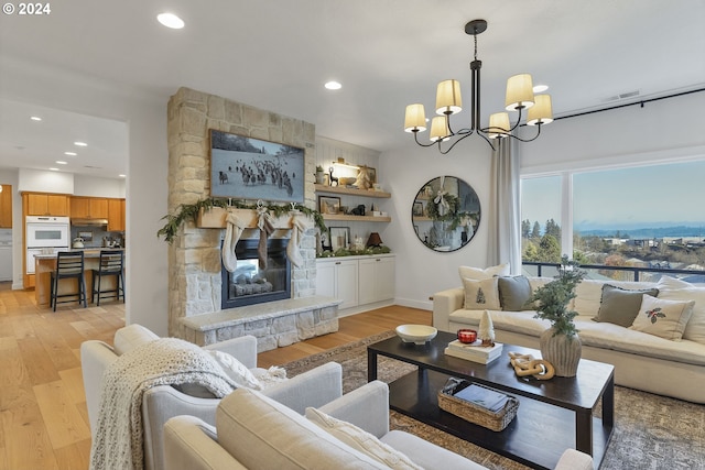 living room with a stone fireplace, light hardwood / wood-style floors, and a notable chandelier