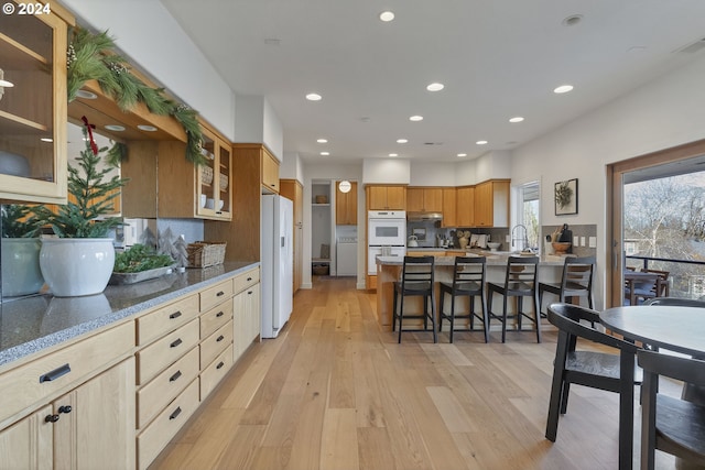 kitchen featuring backsplash, white appliances, a breakfast bar area, and light hardwood / wood-style flooring