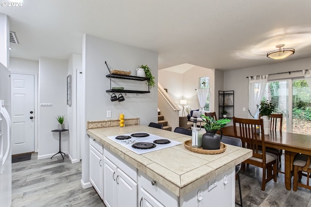 kitchen featuring a kitchen breakfast bar, tile counters, white cabinets, white electric stovetop, and light wood-type flooring