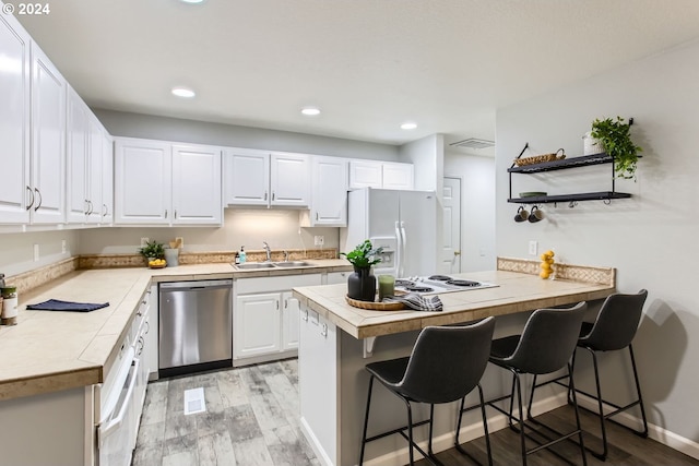 kitchen with sink, a breakfast bar area, kitchen peninsula, white appliances, and white cabinets