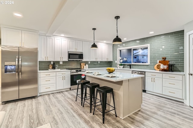 kitchen featuring hanging light fixtures, stainless steel appliances, a kitchen island, backsplash, and white cabinets