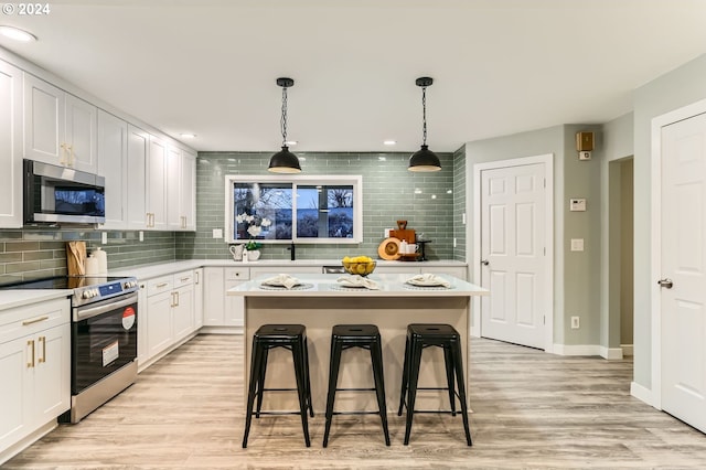 kitchen with a kitchen breakfast bar, light hardwood / wood-style flooring, pendant lighting, white cabinets, and appliances with stainless steel finishes