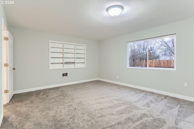 empty room with built in shelves, carpet floors, and a textured ceiling