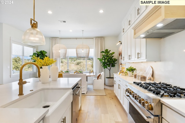 kitchen with premium range hood, stainless steel appliances, sink, and pendant lighting