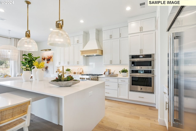 kitchen with custom exhaust hood, stainless steel appliances, white cabinets, and decorative light fixtures