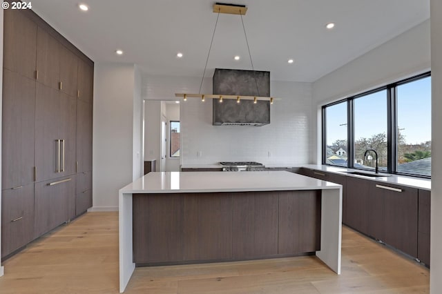 kitchen with dark brown cabinetry, a center island, sink, light hardwood / wood-style flooring, and backsplash