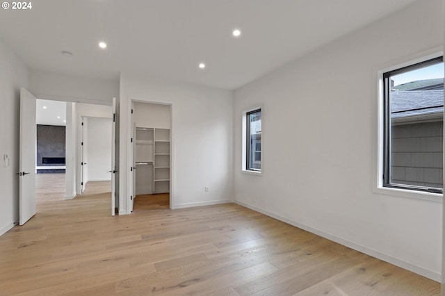 unfurnished bedroom with light hardwood / wood-style floors, a walk in closet, a fireplace, and a closet