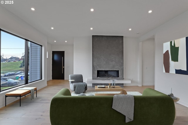 living area with baseboards, light wood-style floors, a large fireplace, and recessed lighting