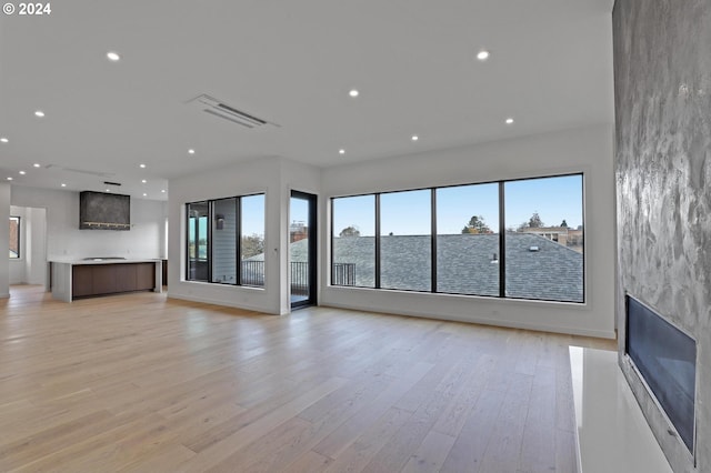 unfurnished living room featuring light wood-type flooring, a water view, and a healthy amount of sunlight