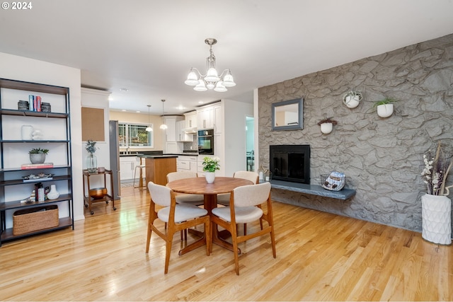 dining space featuring light hardwood / wood-style floors, a notable chandelier, and a stone fireplace