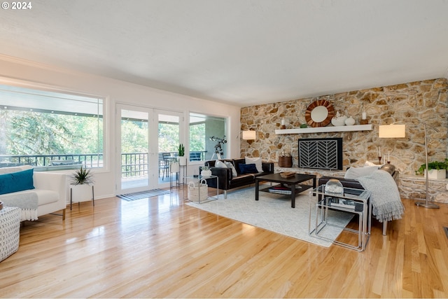 living room with french doors, a stone fireplace, and light wood-type flooring