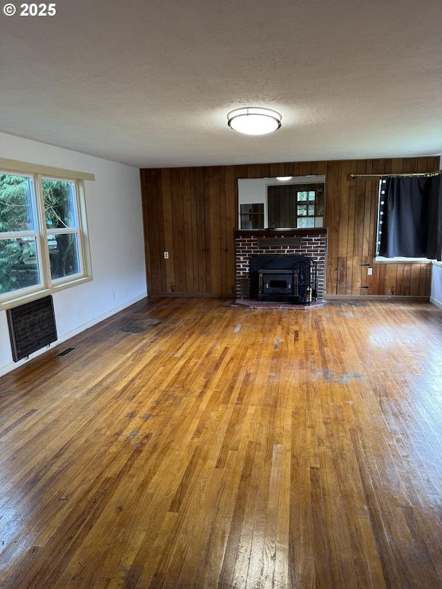 unfurnished living room featuring a brick fireplace, a textured ceiling, heating unit, wood-type flooring, and wood walls