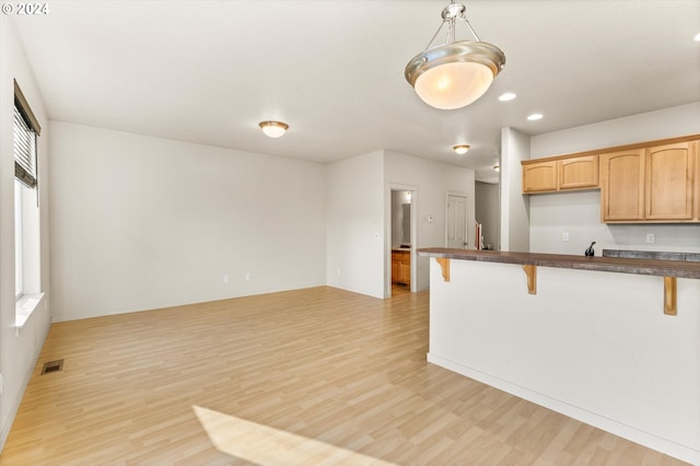 kitchen featuring pendant lighting, light brown cabinets, light hardwood / wood-style floors, a kitchen bar, and kitchen peninsula