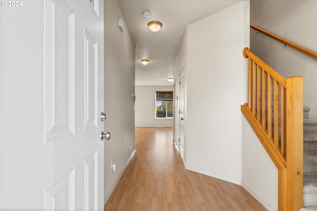 hall with a textured ceiling and light wood-type flooring