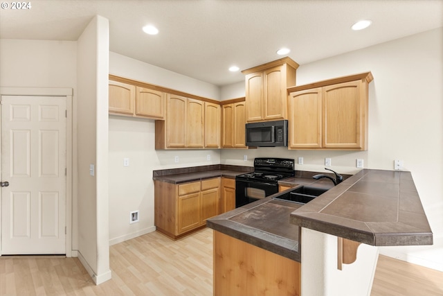 kitchen featuring black appliances, a kitchen breakfast bar, sink, light hardwood / wood-style flooring, and kitchen peninsula