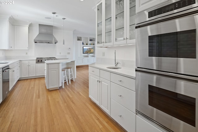 2868 NW Cumberland Rd, Portland, OR 97210 - kitchen with wall chimney range hood, appliances with stainless steel finishes, light wood-style flooring, a kitchen bar, and light countertops