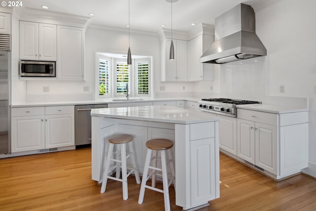 2868 NW Cumberland Rd, Portland, OR 97210 - kitchen featuring built in appliances, wall chimney range hood, light wood-type flooring, white cabinets, and ornamental molding