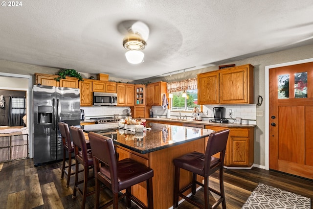 kitchen featuring stainless steel microwave, fridge with ice dispenser, brown cabinets, and dark wood-style flooring