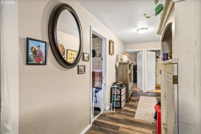 hall featuring baseboards, a textured ceiling, a textured wall, and wood finished floors