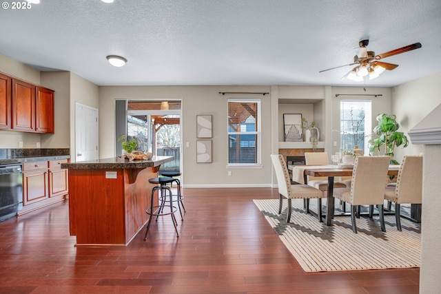 dining room featuring ceiling fan, dark hardwood / wood-style floors, a tiled fireplace, and a textured ceiling