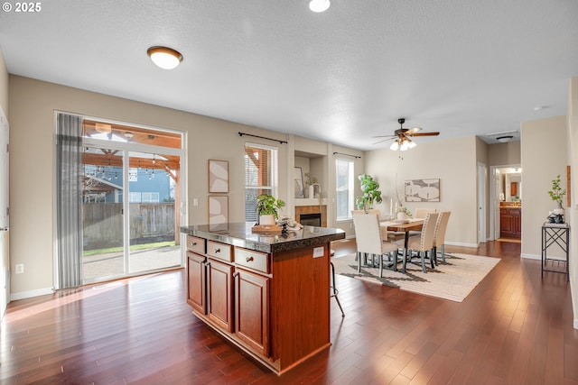 kitchen featuring a tiled fireplace, dark wood-type flooring, a kitchen breakfast bar, and a center island