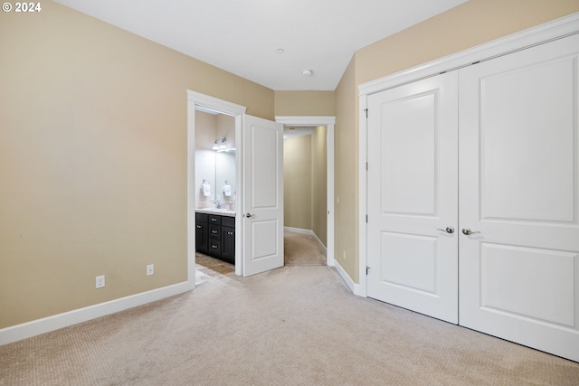 unfurnished bedroom with a closet, light colored carpet, connected bathroom, and sink