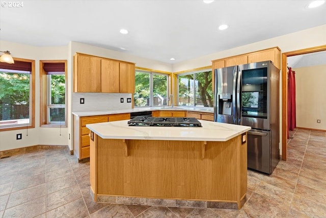 kitchen with gas cooktop, decorative backsplash, stainless steel refrigerator with ice dispenser, a kitchen bar, and a center island