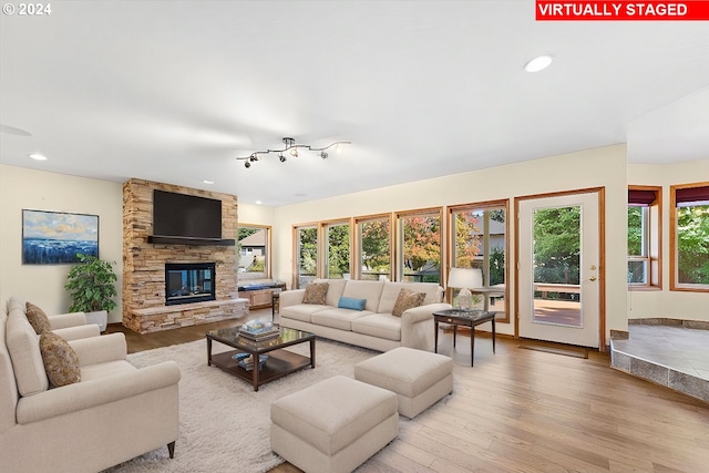 living room featuring a healthy amount of sunlight, a stone fireplace, and light hardwood / wood-style flooring