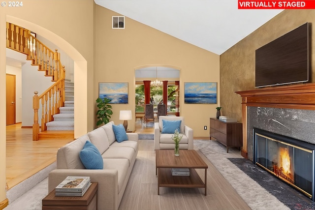 living room featuring a premium fireplace, high vaulted ceiling, an inviting chandelier, and light hardwood / wood-style floors