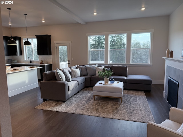 living room featuring a tile fireplace, beam ceiling, dark wood-type flooring, and sink