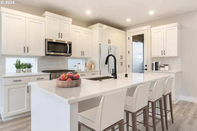 kitchen with decorative backsplash, light wood-type flooring, stainless steel appliances, a kitchen island with sink, and white cabinetry