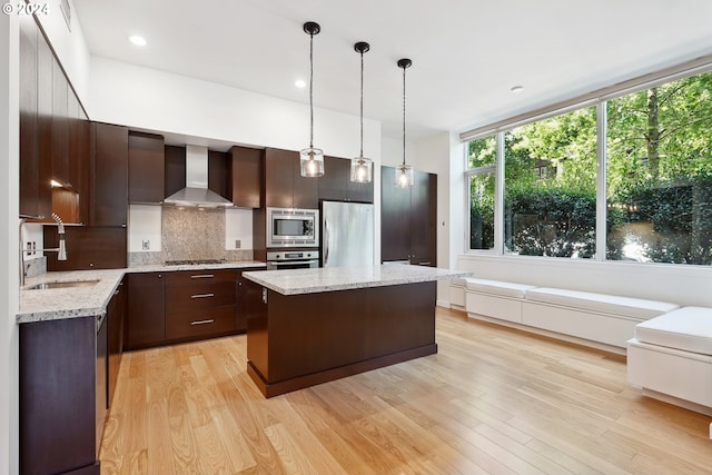 kitchen with light hardwood / wood-style flooring, stainless steel appliances, wall chimney range hood, and a kitchen island