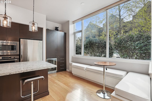 kitchen with light stone counters, stainless steel appliances, light hardwood / wood-style floors, hanging light fixtures, and dark brown cabinets