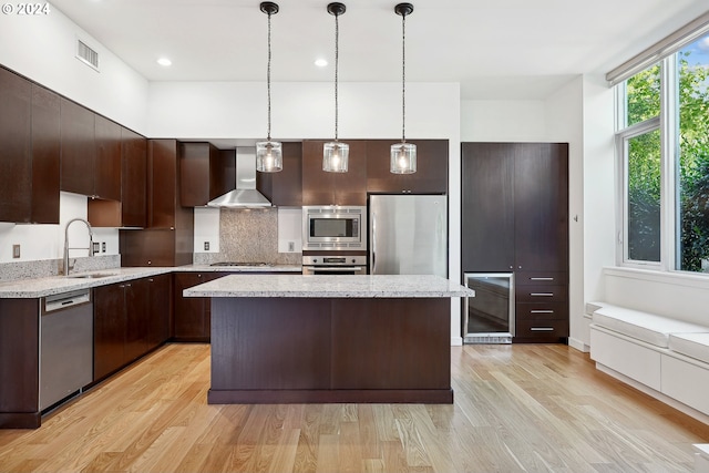 kitchen with appliances with stainless steel finishes, wall chimney exhaust hood, a center island, and light hardwood / wood-style floors