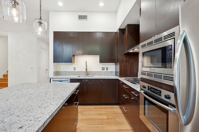 kitchen featuring light hardwood / wood-style floors, decorative light fixtures, sink, light stone counters, and stainless steel appliances