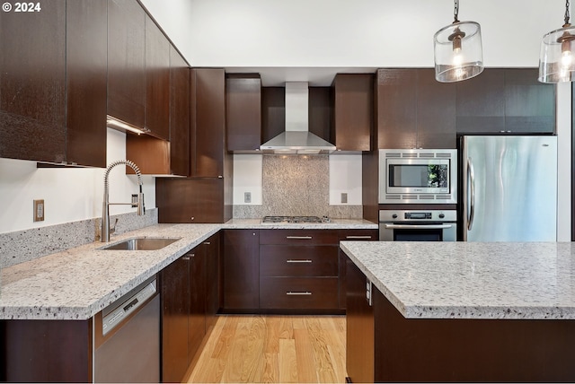 kitchen featuring hanging light fixtures, sink, wall chimney range hood, appliances with stainless steel finishes, and light hardwood / wood-style floors