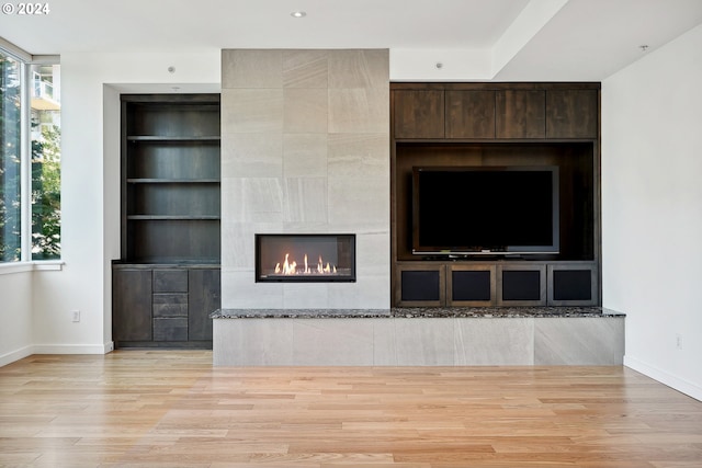 unfurnished living room with a fireplace, built in shelves, and light hardwood / wood-style flooring