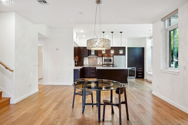 kitchen featuring pendant lighting, a kitchen island, dark brown cabinets, wall chimney exhaust hood, and stainless steel appliances