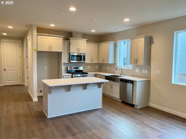 kitchen with sink, white cabinetry, stainless steel appliances, a kitchen island, and decorative backsplash