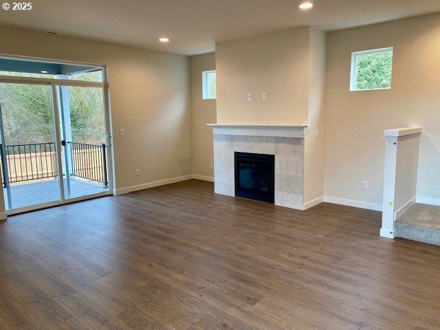 unfurnished living room with dark wood-type flooring, a tile fireplace, and a wealth of natural light