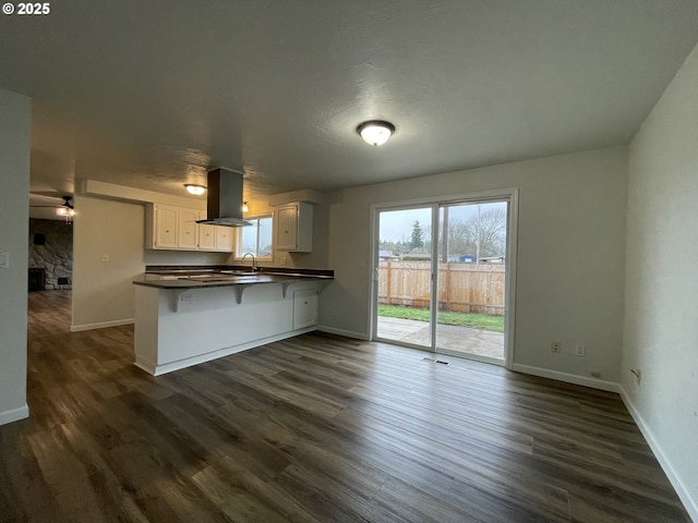 kitchen featuring white cabinetry, dark hardwood / wood-style flooring, island range hood, kitchen peninsula, and a breakfast bar