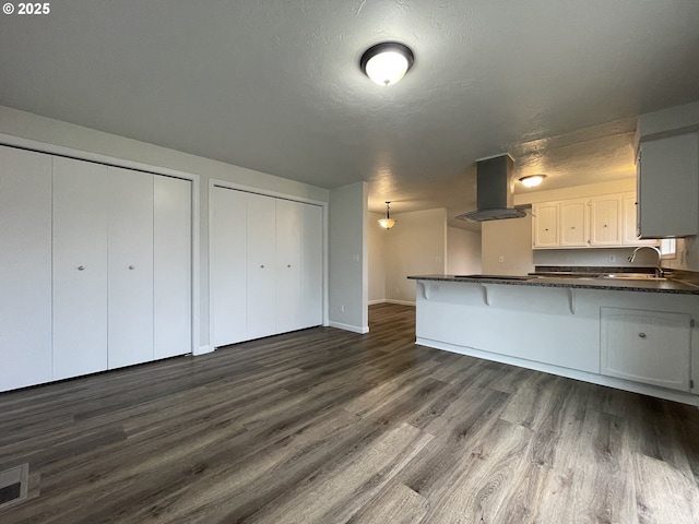 kitchen featuring dark hardwood / wood-style floors, kitchen peninsula, sink, island exhaust hood, and white cabinets