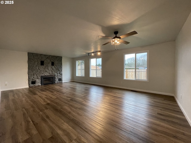 unfurnished living room featuring ceiling fan, dark hardwood / wood-style flooring, a stone fireplace, and track lighting