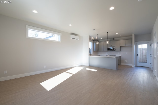 unfurnished living room featuring an AC wall unit, an inviting chandelier, and light hardwood / wood-style floors