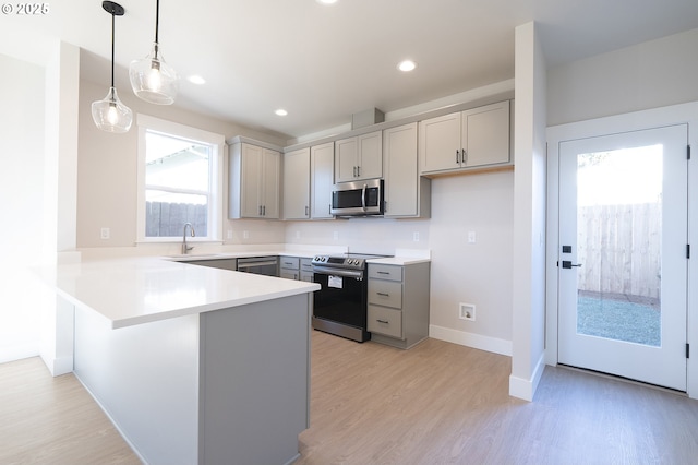 kitchen with sink, gray cabinets, stainless steel appliances, decorative light fixtures, and light wood-type flooring