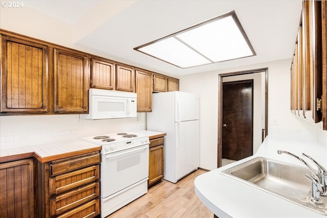 kitchen with tile counters, sink, white appliances, and light hardwood / wood-style flooring